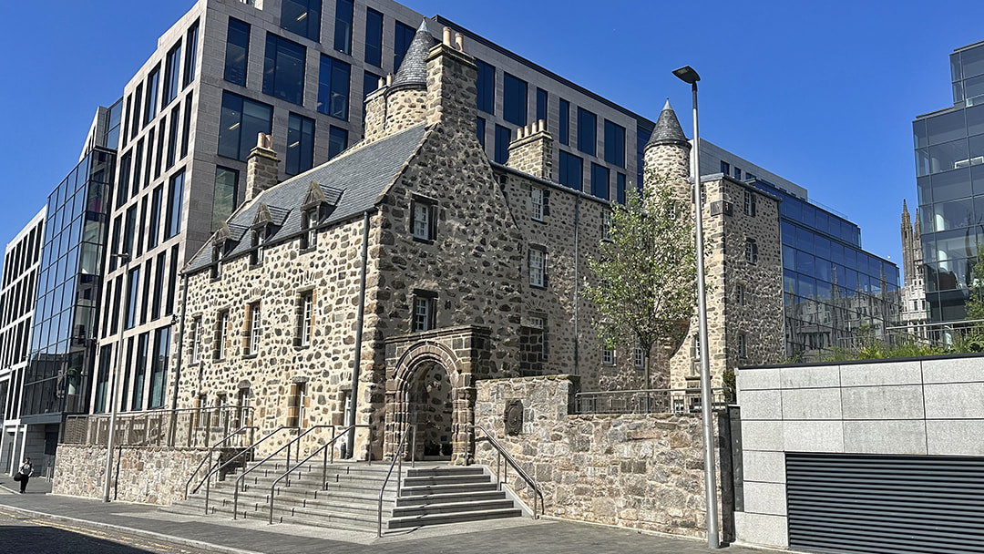 Old-fashioned Provost Skene House nestled between modern buildings, as seen from Flourmill Lane