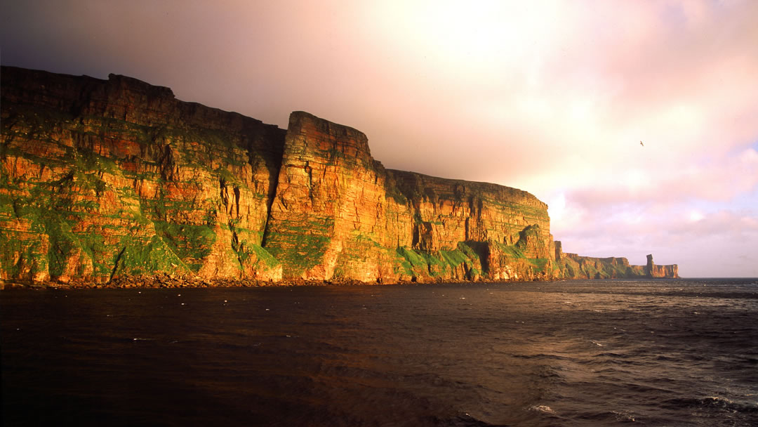 The setting sun against St Johns Head and the Old Man of Hoy