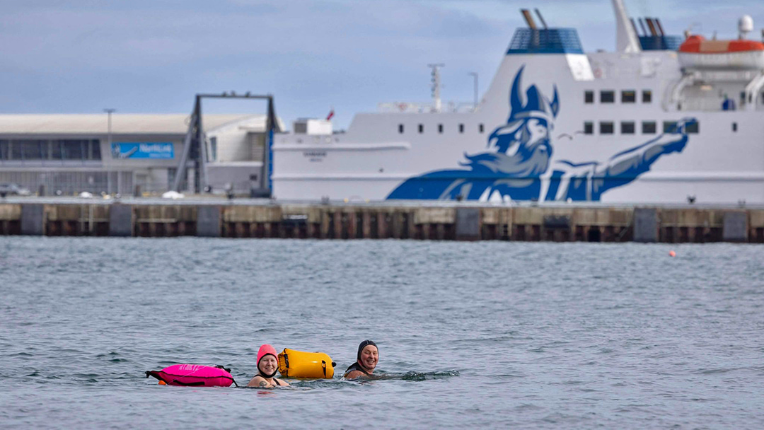 Nicola Mowat and Chris Parkinson swimming in the Pentland Firth in front of the MV Hamnavoe